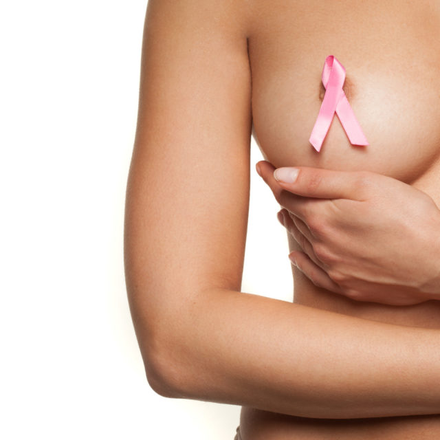 Naked woman wearing a pink breast cancer ribbon attached to her bare nipple as she cups her breast with her hand in a graceful movement, isolated on white